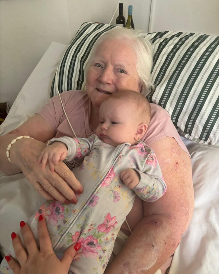 Elderly woman lying in bed holding a baby, both relaxed and close together.