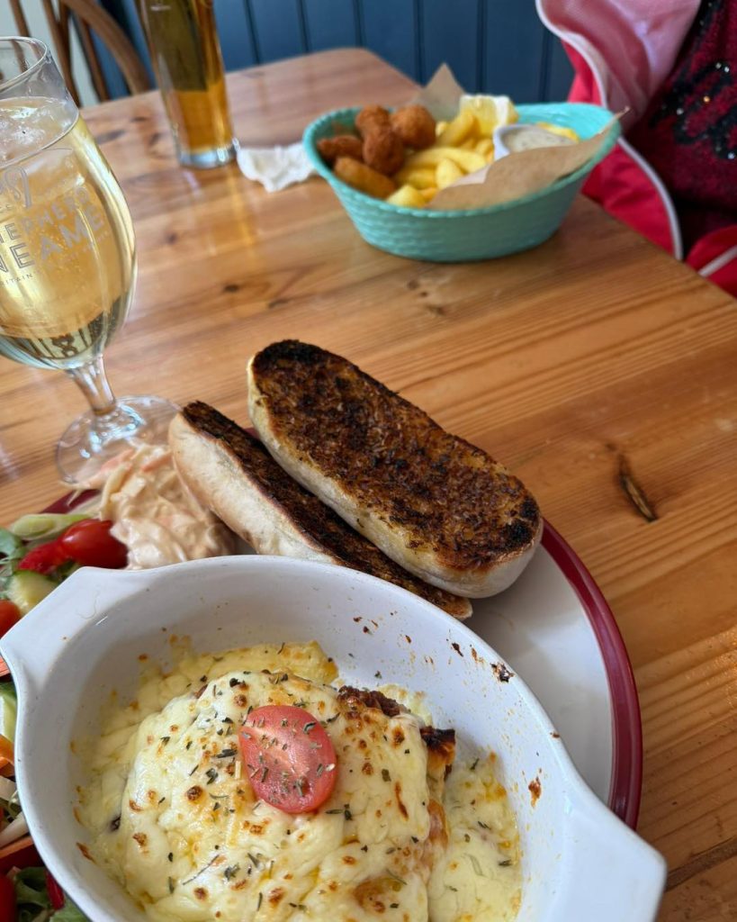 Cheesy baked dish with toast, salad, and a glass of white wine on a wooden table.