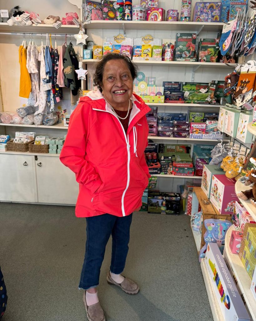 Smiling woman in a red jacket standing inside a colorful gift shop.