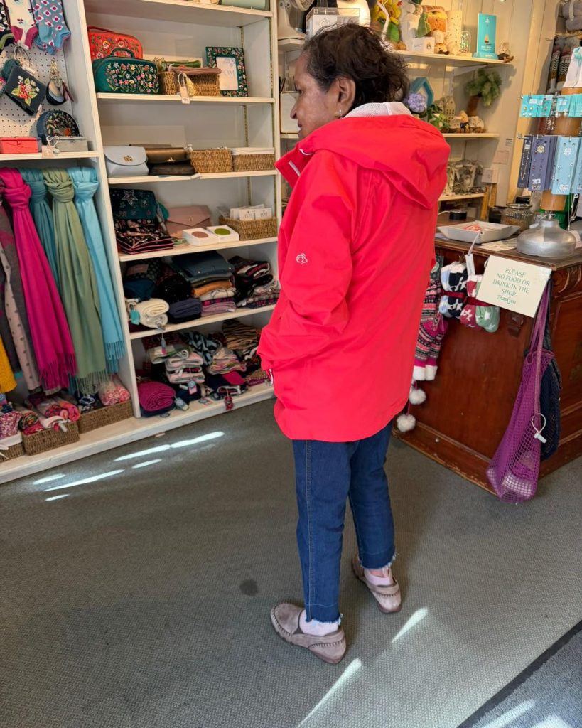 Woman in a bright red jacket standing in a gift shop, facing shelves of accessories.