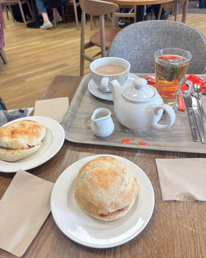 Tray with tea, teapot, and two sandwiches on a café table.