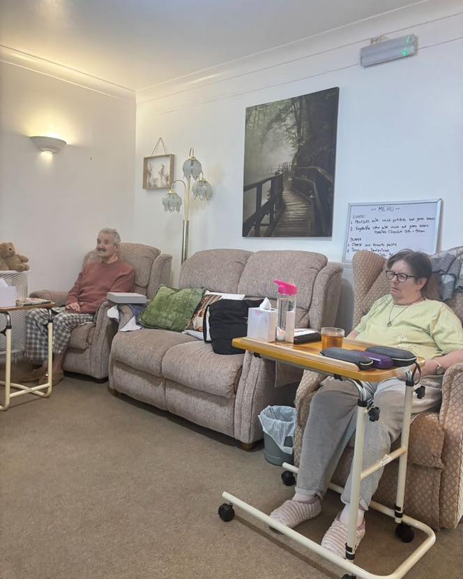 Two residents relaxing in armchairs in a quiet shared living room.