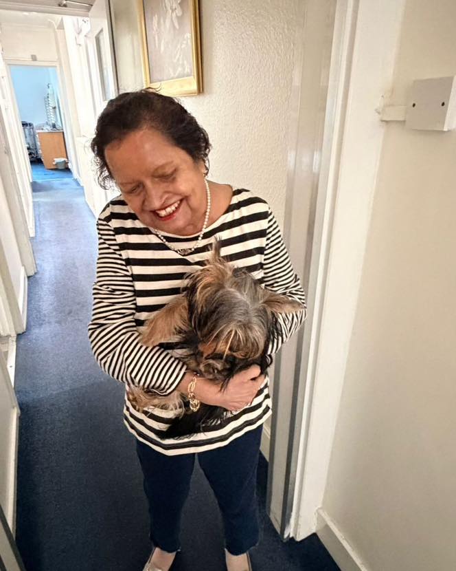 Smiling woman in a striped top holding a small dog in a hallway.