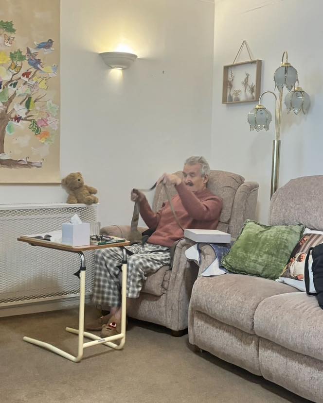 Elderly man sitting in an armchair holding a strap in a cozy lounge area.