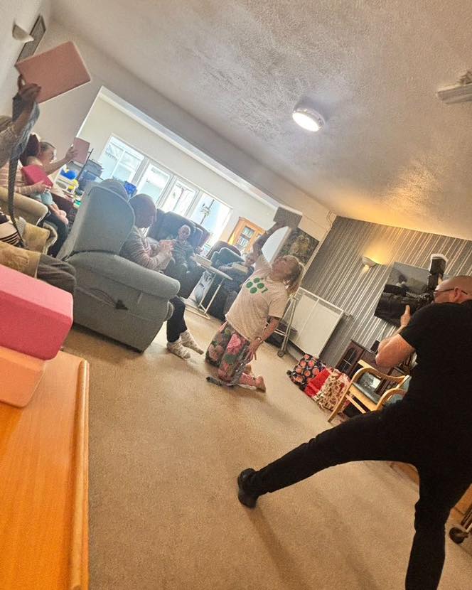 Activity leader kneeling in front of seated residents while a photographer captures the session.