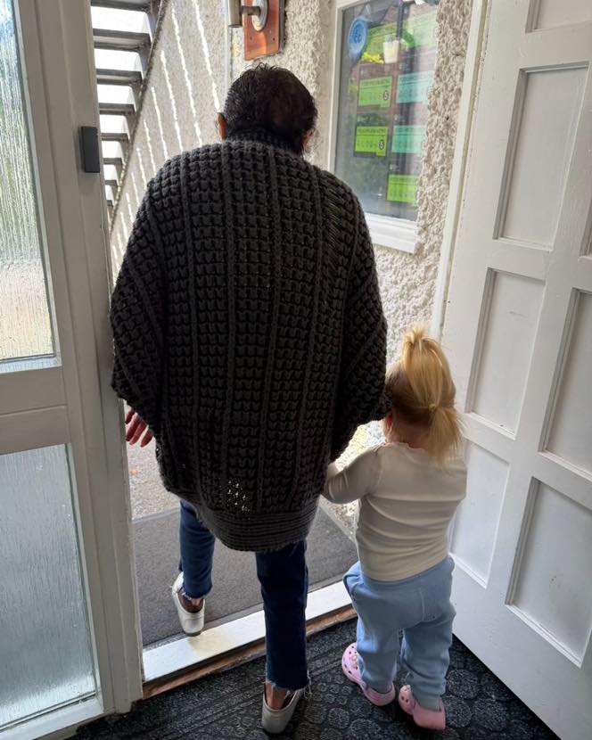 Adult and young child holding hands while stepping out of a doorway.