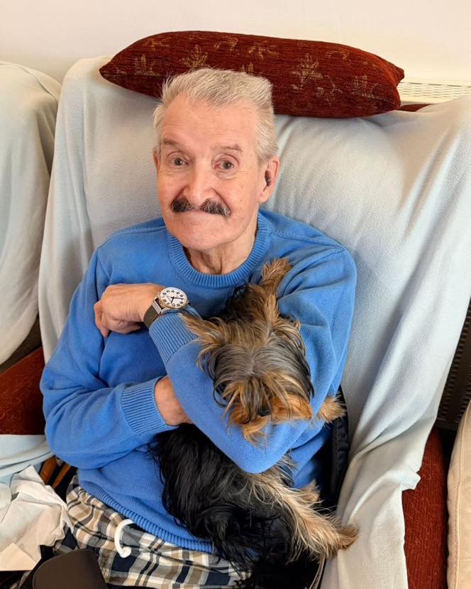 Older man sitting in a chair holding a small dog in his arms.