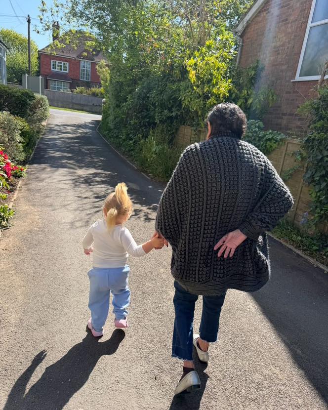 Adult and child walking hand-in-hand down a sunny residential path.