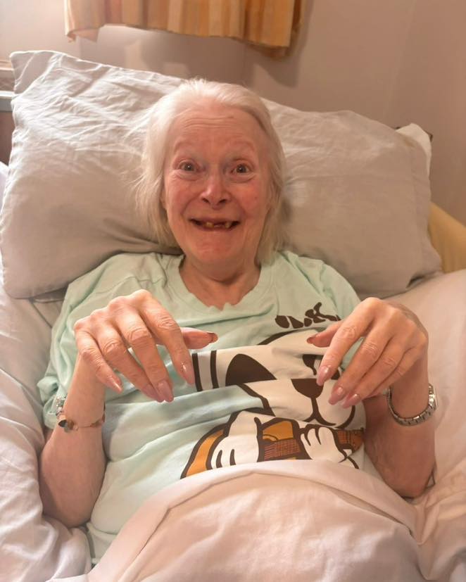 Smiling elderly woman sitting comfortably in bed, proudly displaying her manicured nails.