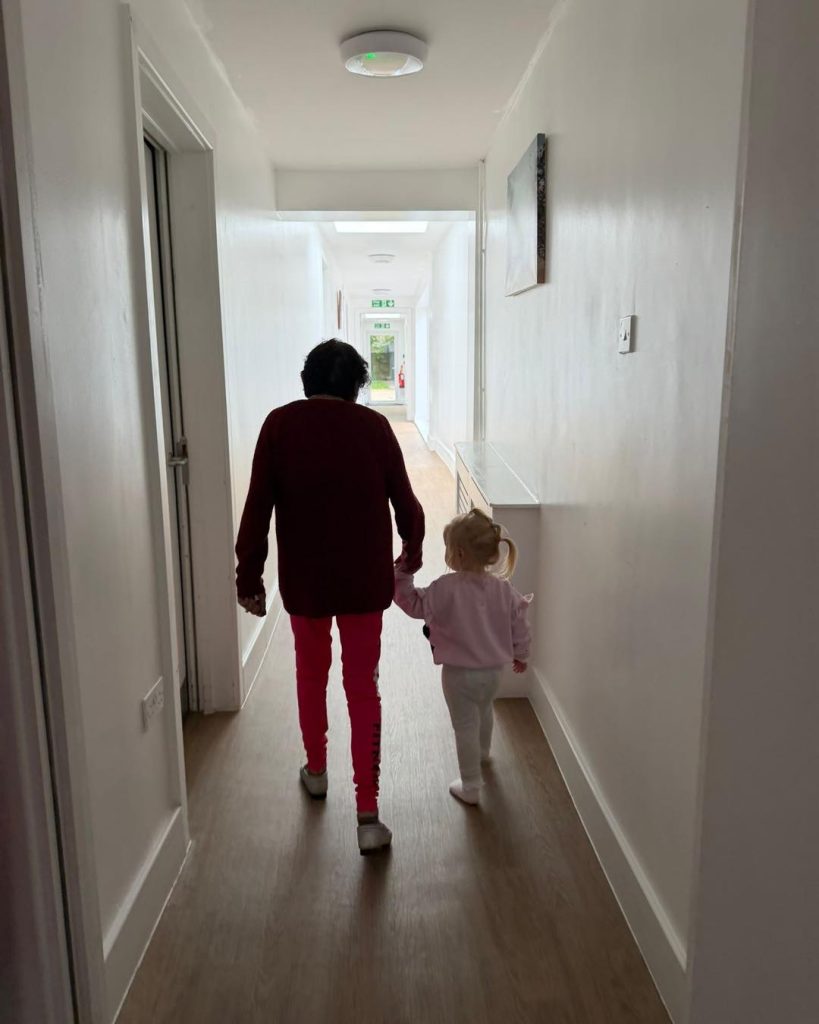 Elderly resident and young child walking hand in hand down a care home corridor.