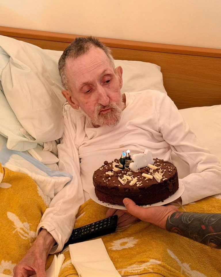 Older man in bed being presented with a birthday cake during a special celebration.