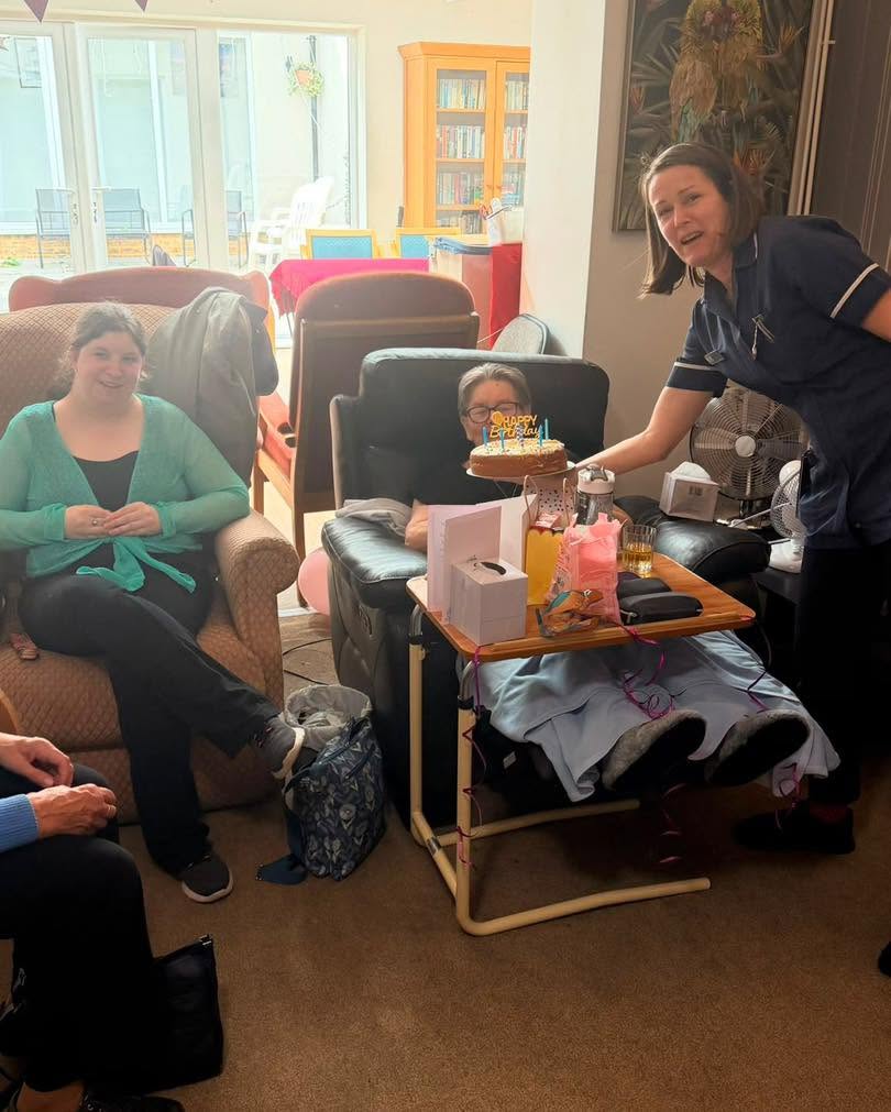 Resident smiles as staff presents a birthday cake and gifts.