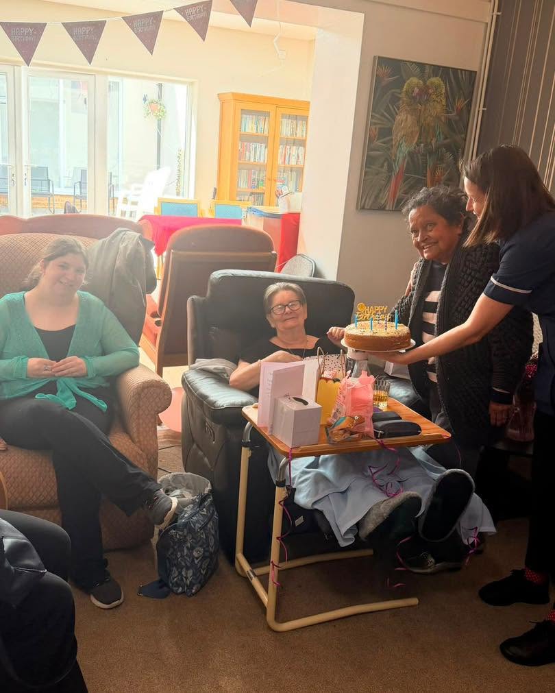 Resident smiles as staff presents a birthday cake surrounded by friends.