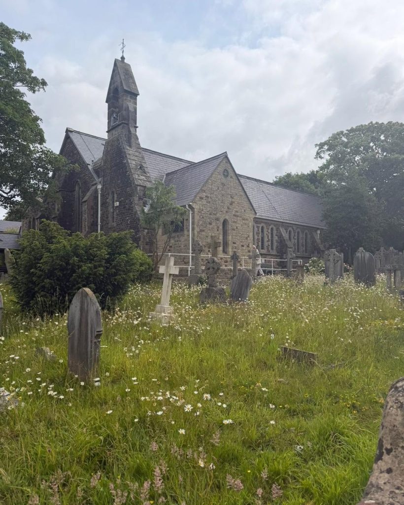 Historic church with gravestones and wildflowers in the churchyard.