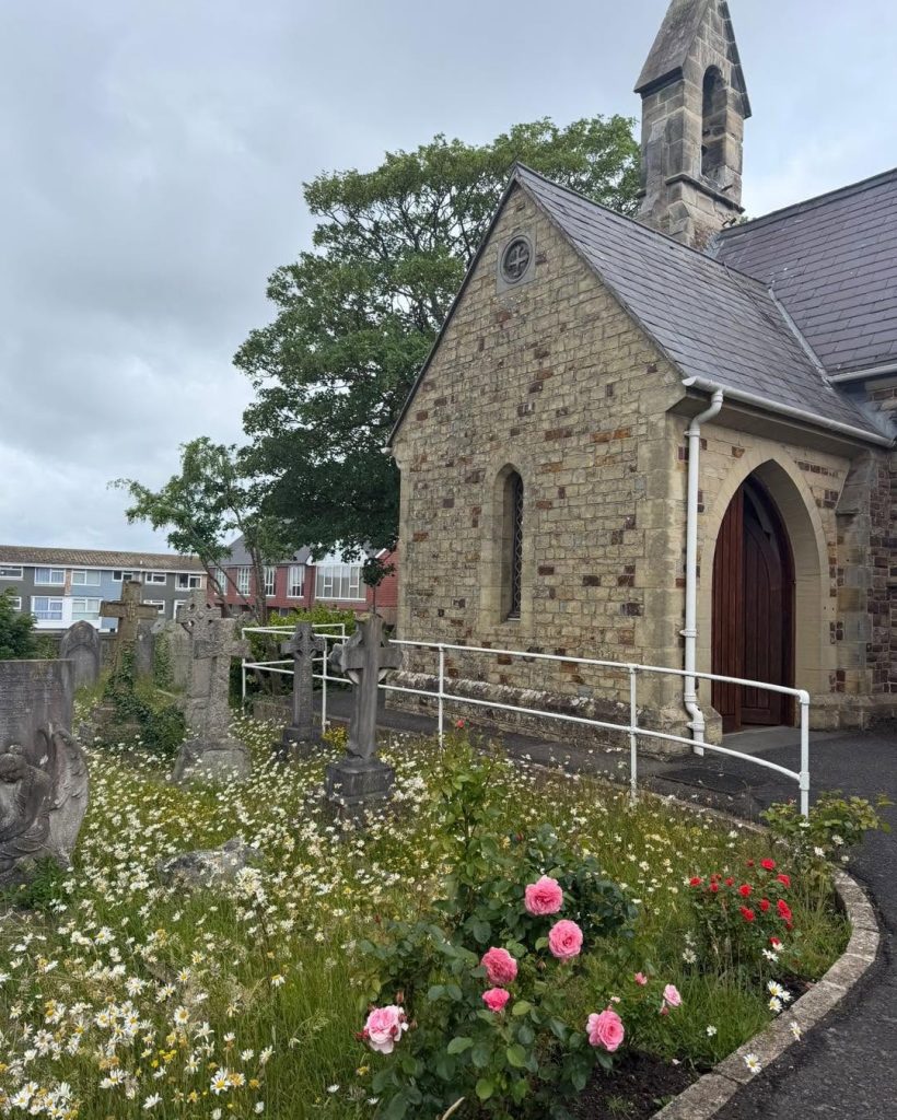Churchyard with stone crosses, flowers, and church building.