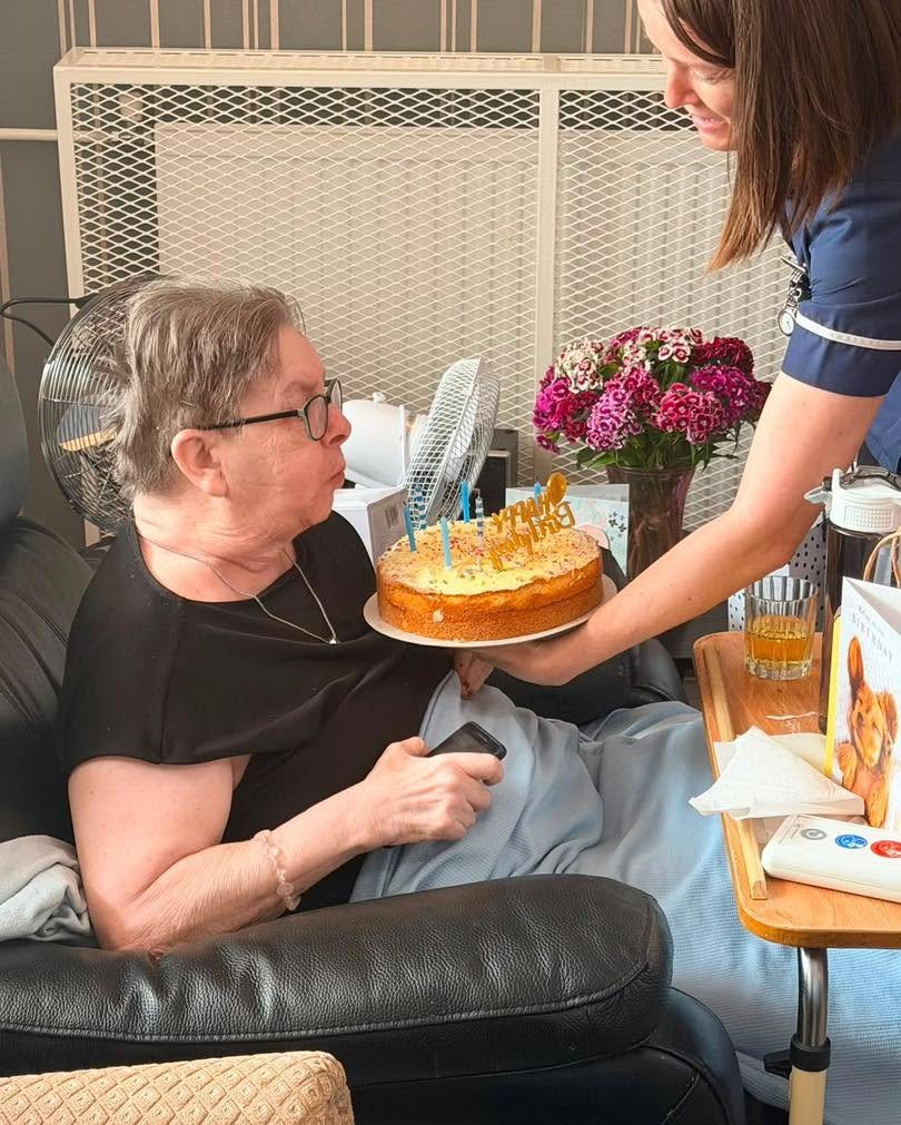 Resident blows out candles on a birthday cake held by staff.