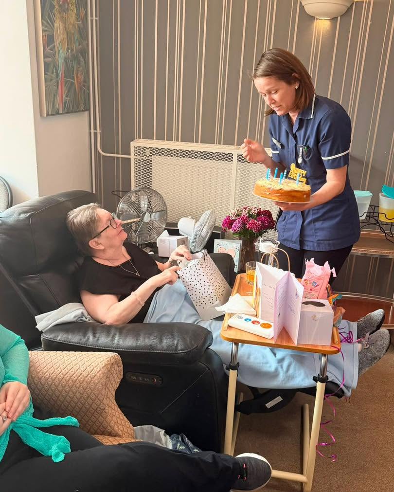 Resident opens a birthday gift while staff holds a cake with candles.