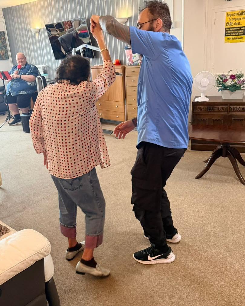 Resident and carer enjoying a joyful dance during a care home activity.