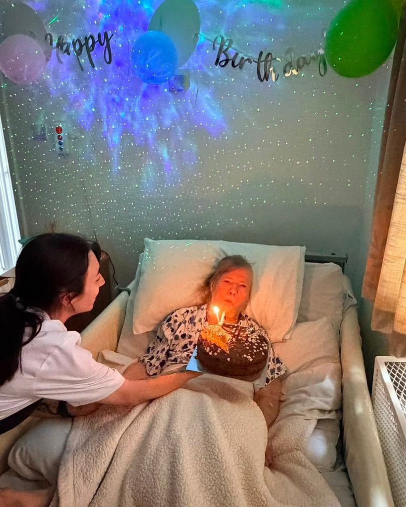 Resident blowing out birthday candles while staff celebrate with a cake in a warm and caring environment.