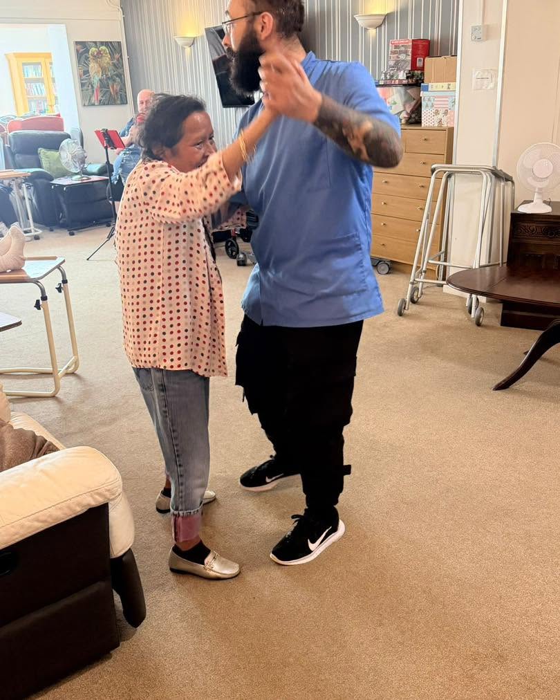 Smiling resident dancing with a care team member in a bright communal lounge.