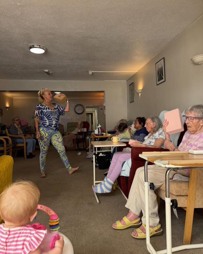 Residents enjoying a fun group activity led by an entertainer in a bright lounge at Hazelmere Nursing Home, with a young child watching nearby.