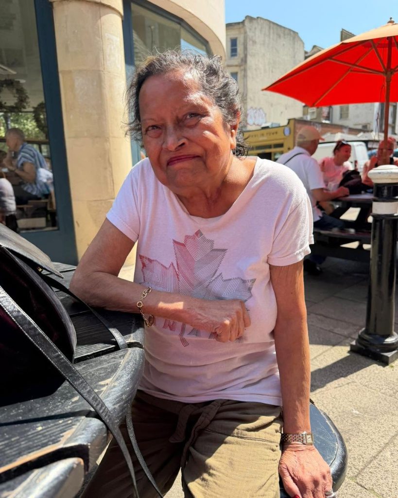 Smiling elderly woman relaxing on a bench outside a café on a sunny day.