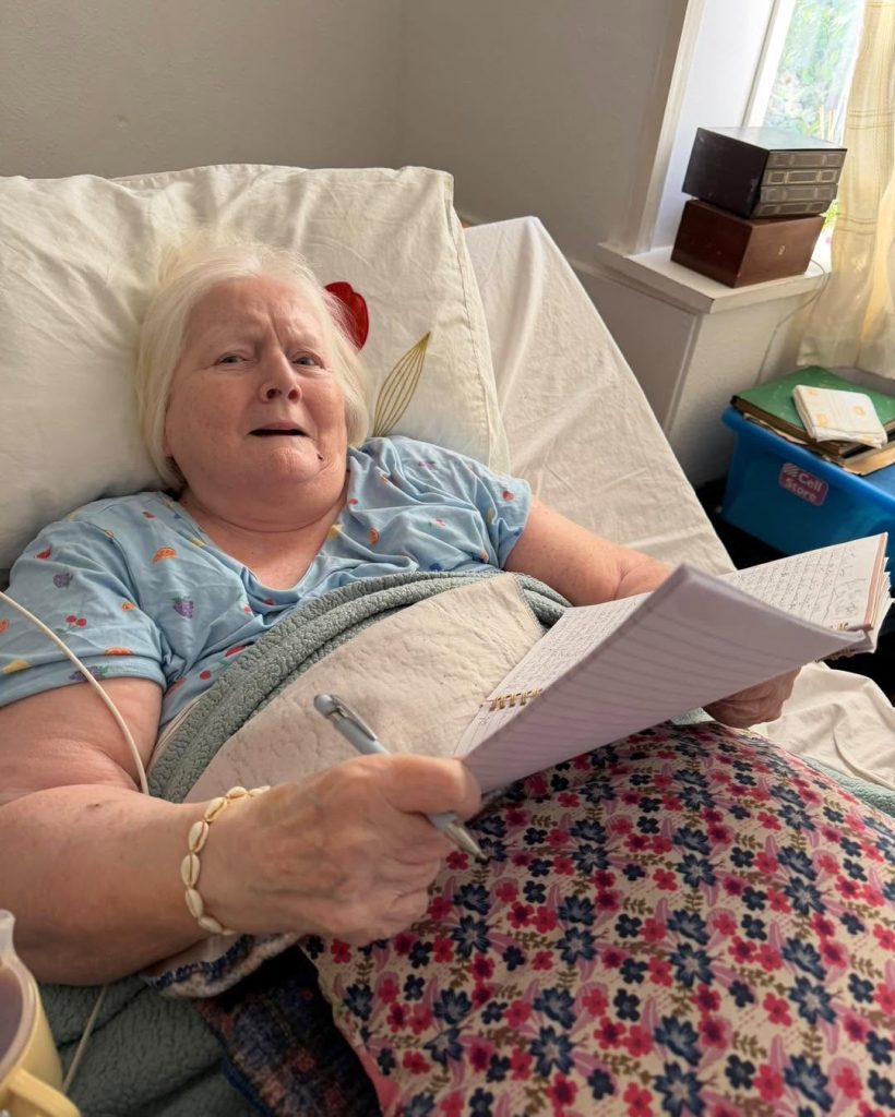 Older woman writing in a notebook in bed.