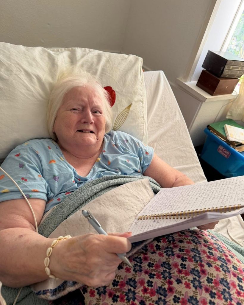 Older woman writing in a notebook while resting in bed.