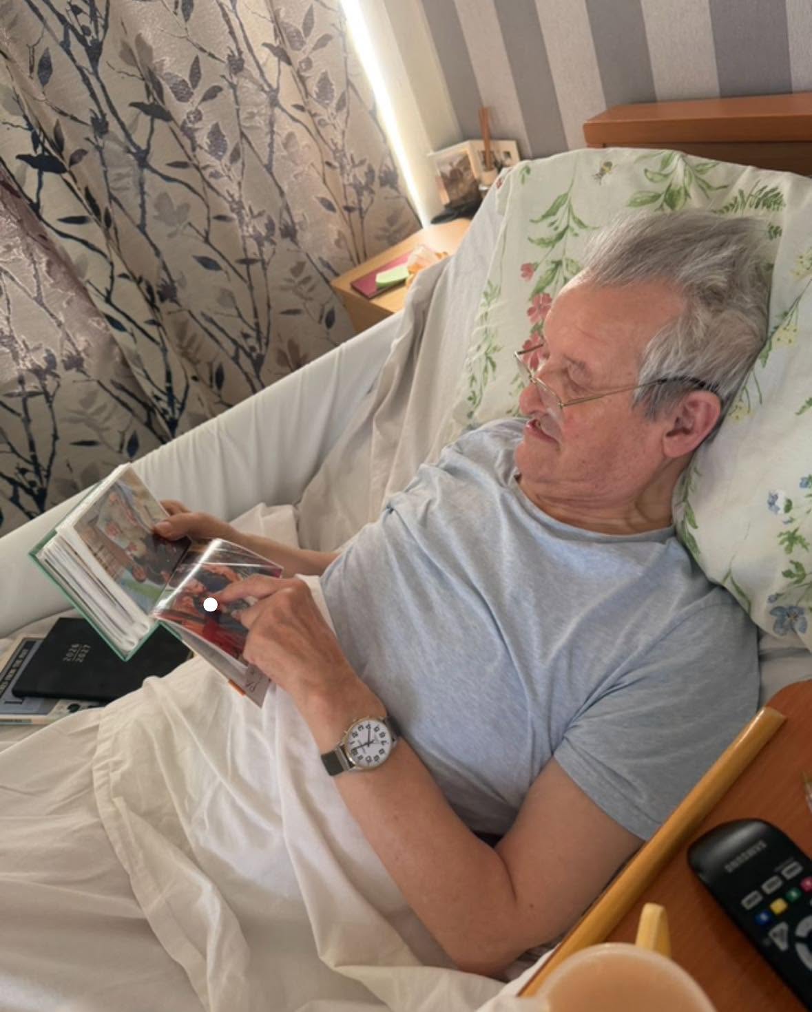 Elderly man reading a family photo album while resting in bed.