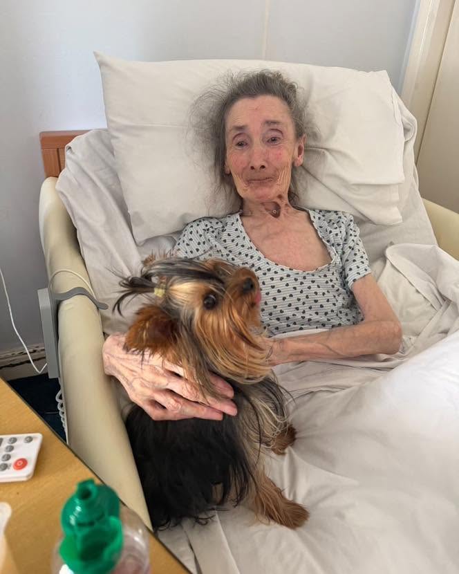 Elderly woman smiling while holding her dog in bed.