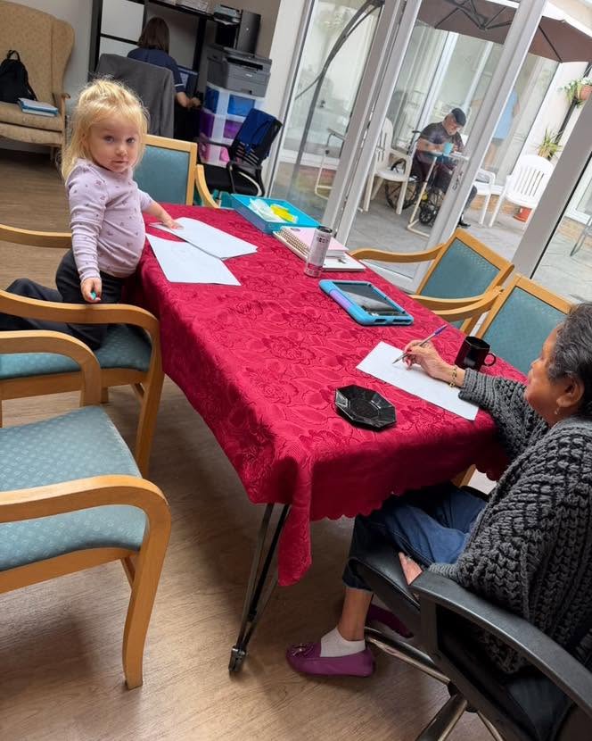 A young girl and an elderly resident enjoy a drawing activity together in a care home.