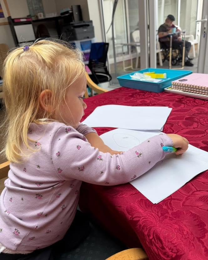 A young girl draws on paper with a colourful marker at a care home activity table.