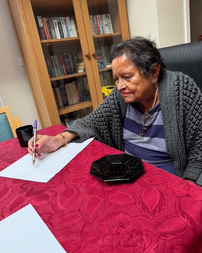 An elderly resident enjoys drawing and writing at a table in a care home.